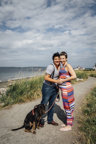 Portrait of pregnant lesbian couple with dog hugging at waterfront