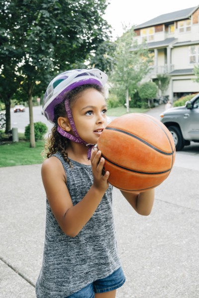 Mixed Race girl wearing helmet playing basketball in driveway