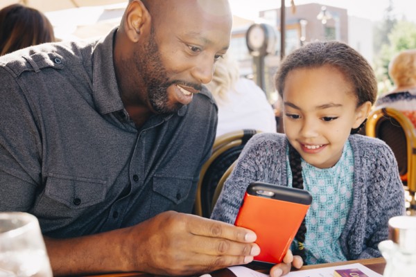 Father and daughter sitting at restaurant table texting on cell phone