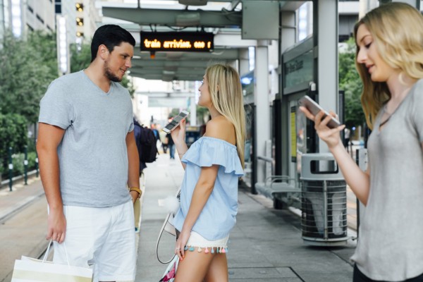 Caucasian woman showing cell phone to man at train station