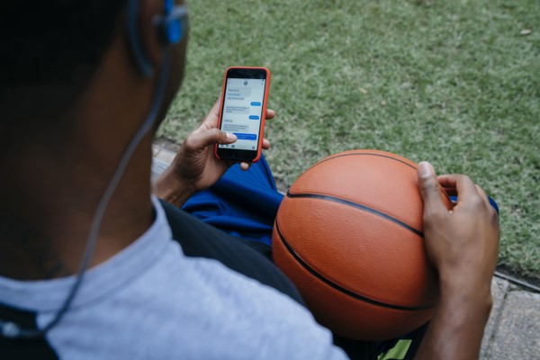 Black man listening to cell phone with earbuds and holding basketball