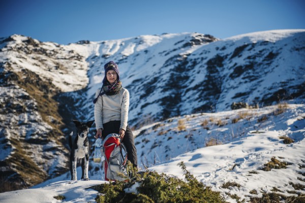 Caucasian woman posing with dog and backpack on mountain