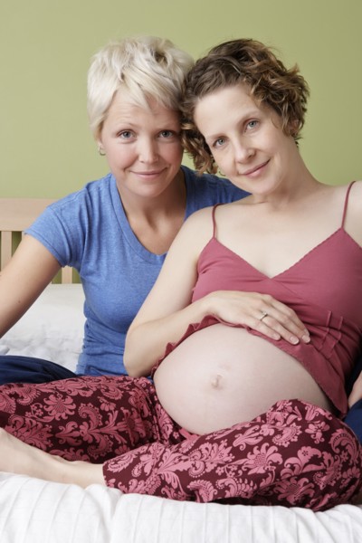Caucasian pregnant lesbian couple relaxing on bed