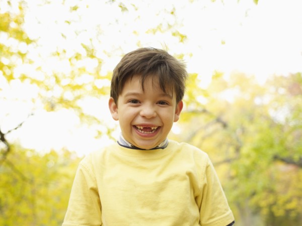 Toothless Hispanic boy grinning outdoors in autumn