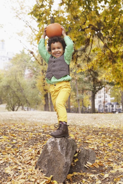 Mixed race boy holding pumpkin overhead in park