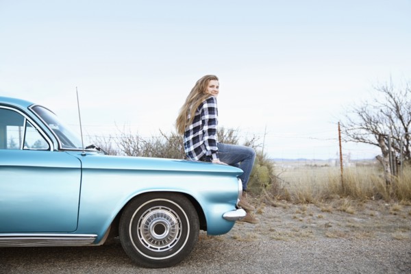 Smiling woman sitting on vintage car