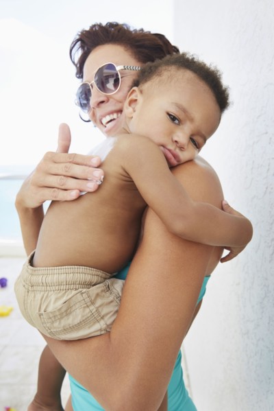 Black mother applying sunscreen to son at beach