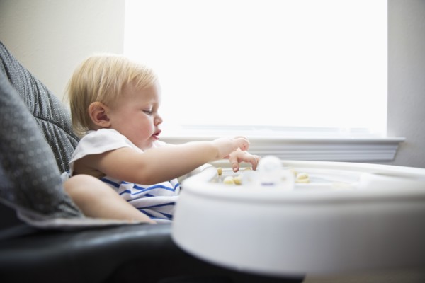 Caucasian baby girl self-feeding in high chair