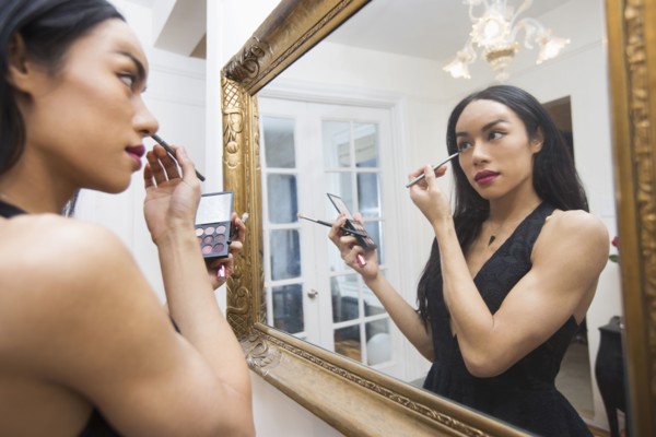 Glamorous transgender Thai woman applying eyeliner in mirror