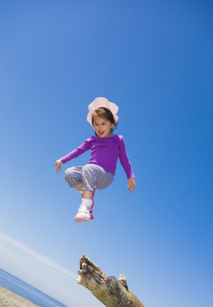 Low angle view of mixed race girl jumping from log on beach