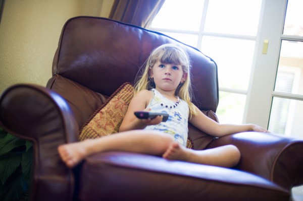 Caucasian girl sitting in armchair holding remote control