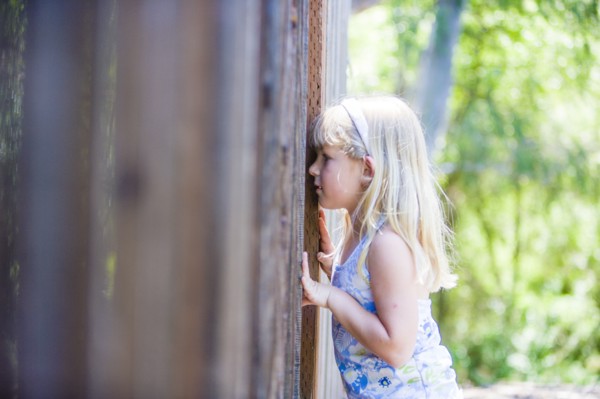 Curious Caucasian girl peeking through wooden fence
