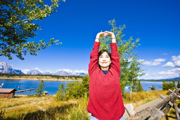 Smiling Japanese woman stretching arms near lake