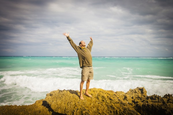 Caucasian man standing on rocks at ocean with arms raised