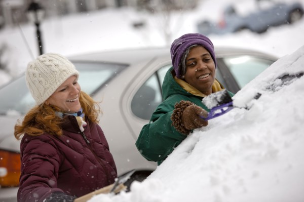 Two women scraping snow from windshield