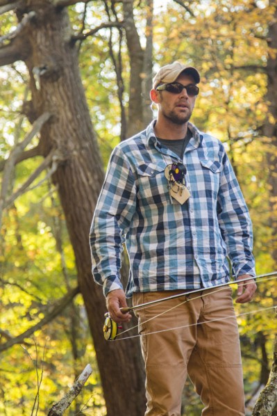 Caucasian man carrying fishing rod under tree