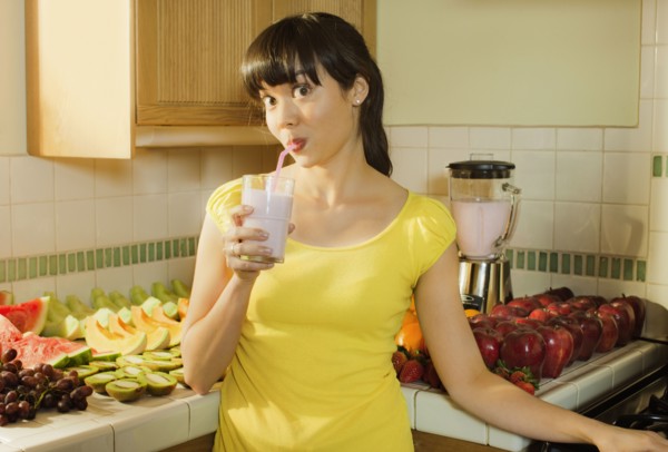 Mixed race woman drinking smoothie in kitchen