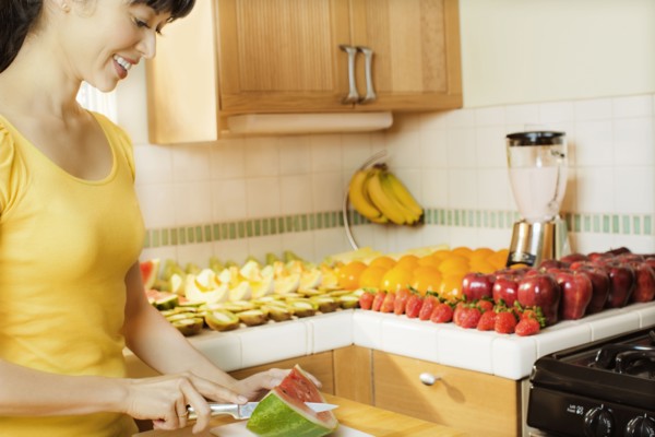 Mixed race woman cutting watermelon in kitchen