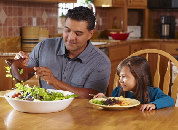 Father serving daughter salad at dinner table