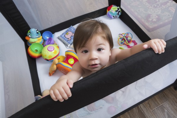 Mixed race baby girl standing in playpen