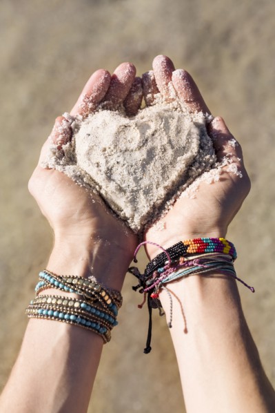 Close up of hands of Caucasian woman holding sand in heart shape