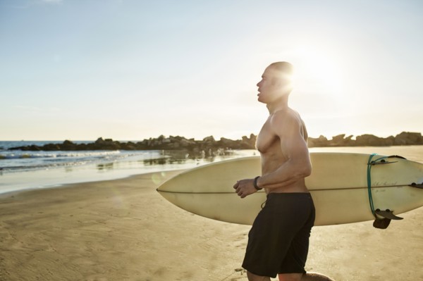 Mixed race man running with surfboard on beach