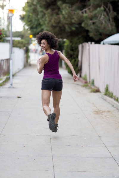 Smiling Mixed Race woman running on sidewalk