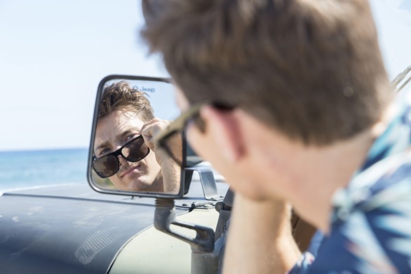 Reflection of Caucasian man in side-view mirror of car on beach