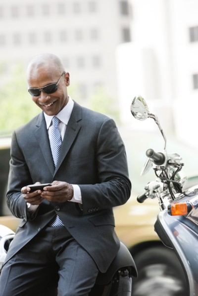 Black businessman sitting on scooter text messaging