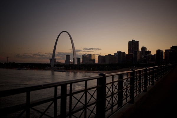 Arch landmark next to urban river at sunset