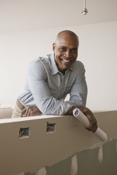 African American man standing in unfinished room with blueprints