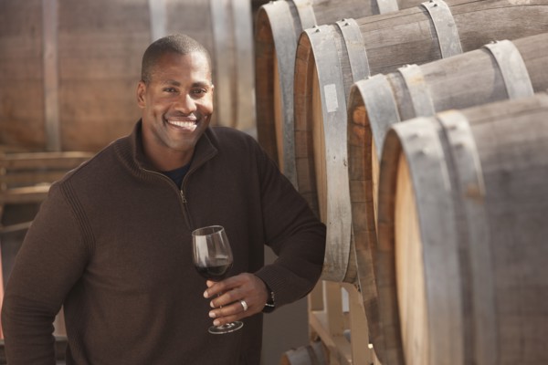 Black man drinking wine near wine barrel