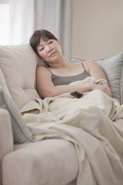 Asian woman laying on sofa watching television
