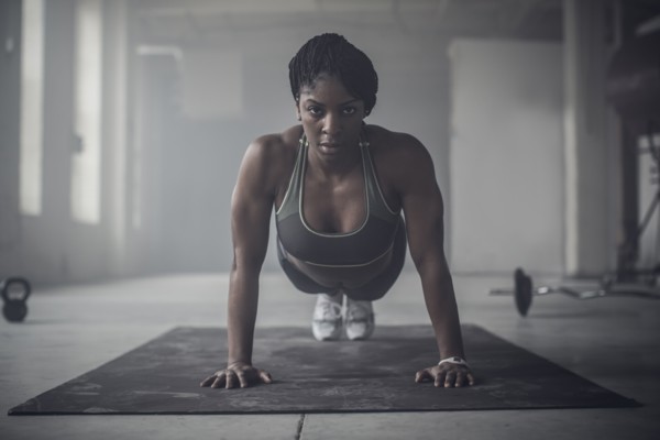 Black woman doing push-ups in dark gym