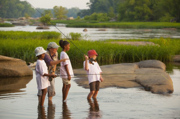 Woman teaching children how to fly fish on river