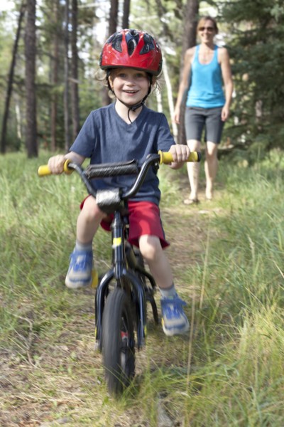 Caucasian mother watching smiling son on bicycle