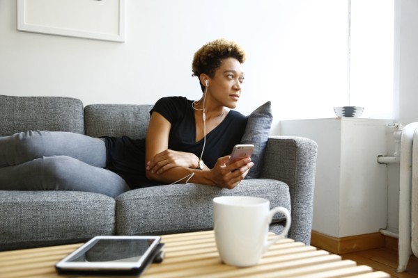 Mixed race woman laying on sofa listening to earbuds