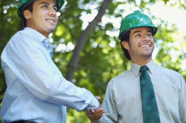 Hispanic businessmen in green hard hats shaking hands outdoors