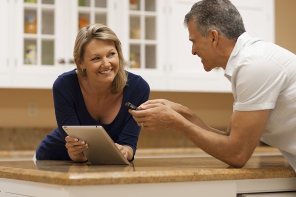 Caucasian couple using digital tablet and cell phone at kitchen counter