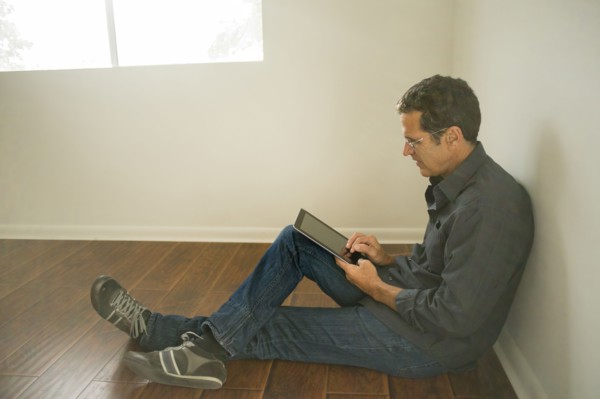 Hispanic man using digital tablet on floor of empty room