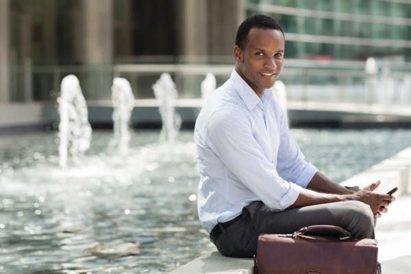 Black businessman using cell phone near urban fountain