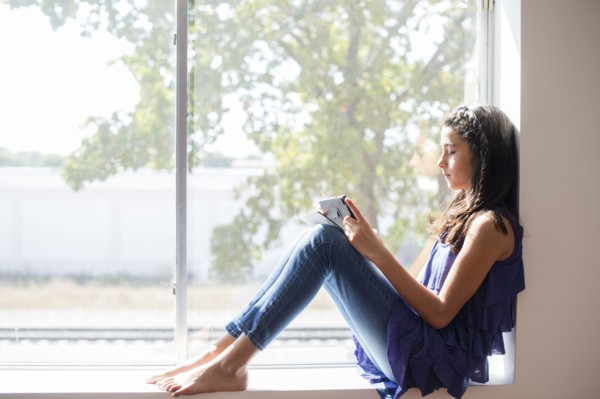 Mixed race girl using digital tablet at window