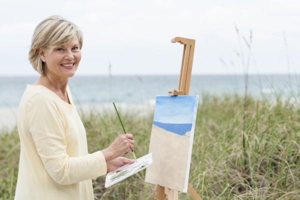 Older Caucasian woman painting beach outdoors