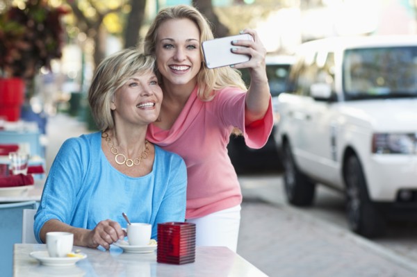 Caucasian mother and daughter taking selfie at sidewalk cafe