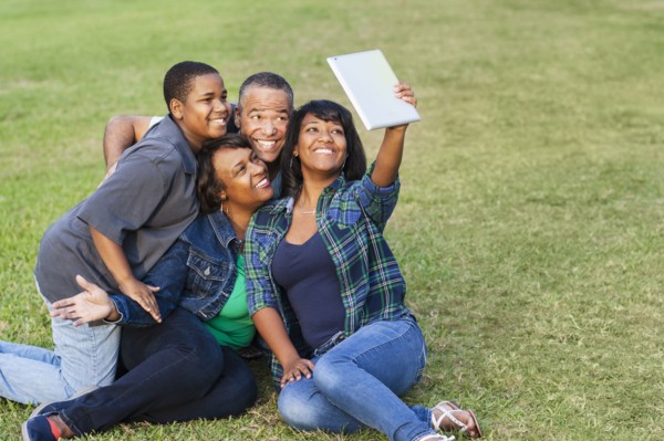 African American family taking selfie with digital tablet on grass