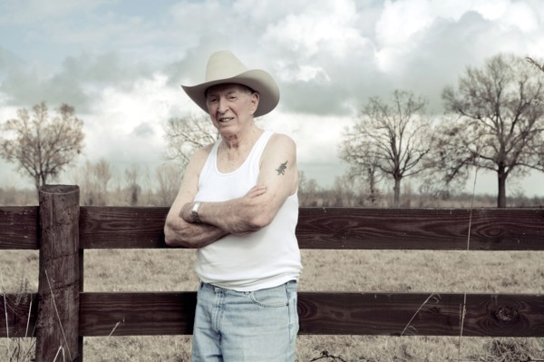 Senior man in cowboy hat standing near wooden fence