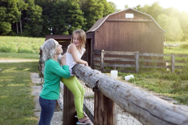 Caucasian grandmother and granddaughter smiling at farm fence