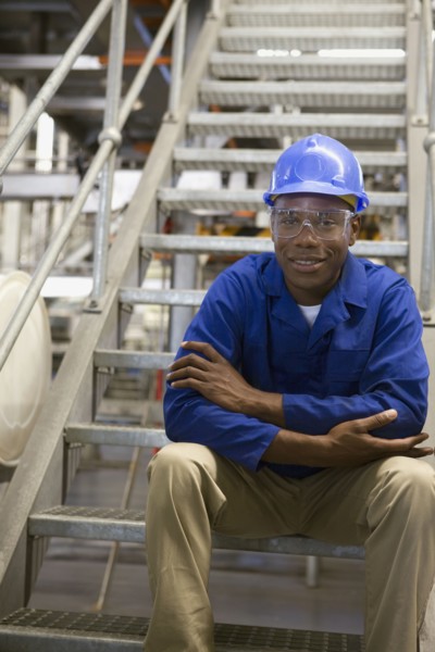African worker in hard-hat sitting on metal staircase