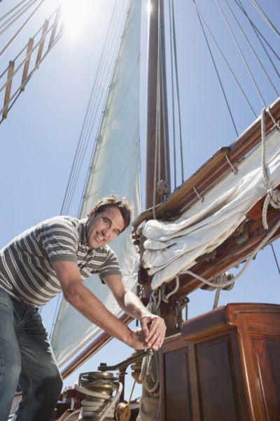 Caucasian man hoisting sail on sailboat