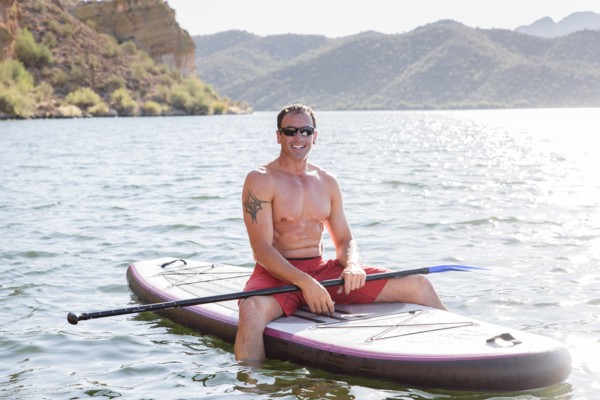 Hispanic man sitting on paddleboard in river